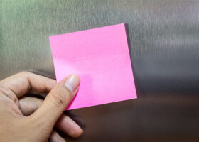 Hand sätter rosa post it-lapp på kylskåp