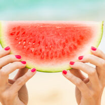 Två händer håller i vattenmelon på strand