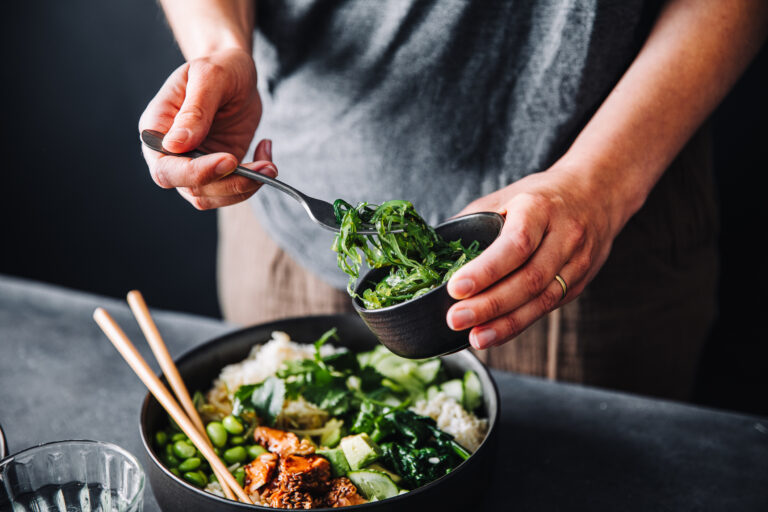 Närbild på person som lägger upp wakame-alger i en skål med sallad