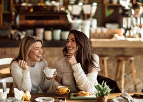 Två kvinnliga vänner skrattar vid ett cafébord