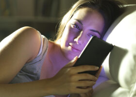 Kvinna i sängen med mobil i handen