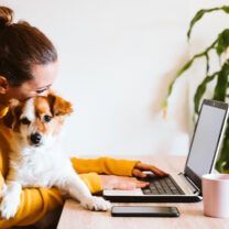 Kvinna jobbar vid dator med hund i famnen