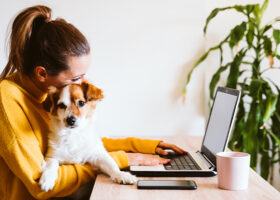 Kvinna jobbar vid dator med hund i famnen