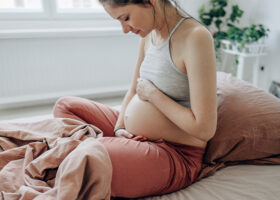 Gravid kvinna håller om sin mage i säng