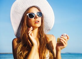 Ung kvinna i solhatt och solglasögon med krämburk i handen