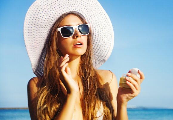 Ung kvinna i solhatt och solglasögon med krämburk i handen