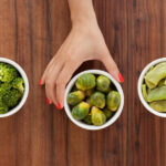 Three bowls with varieties of boiled vegetables and woman's hand holding the middle one