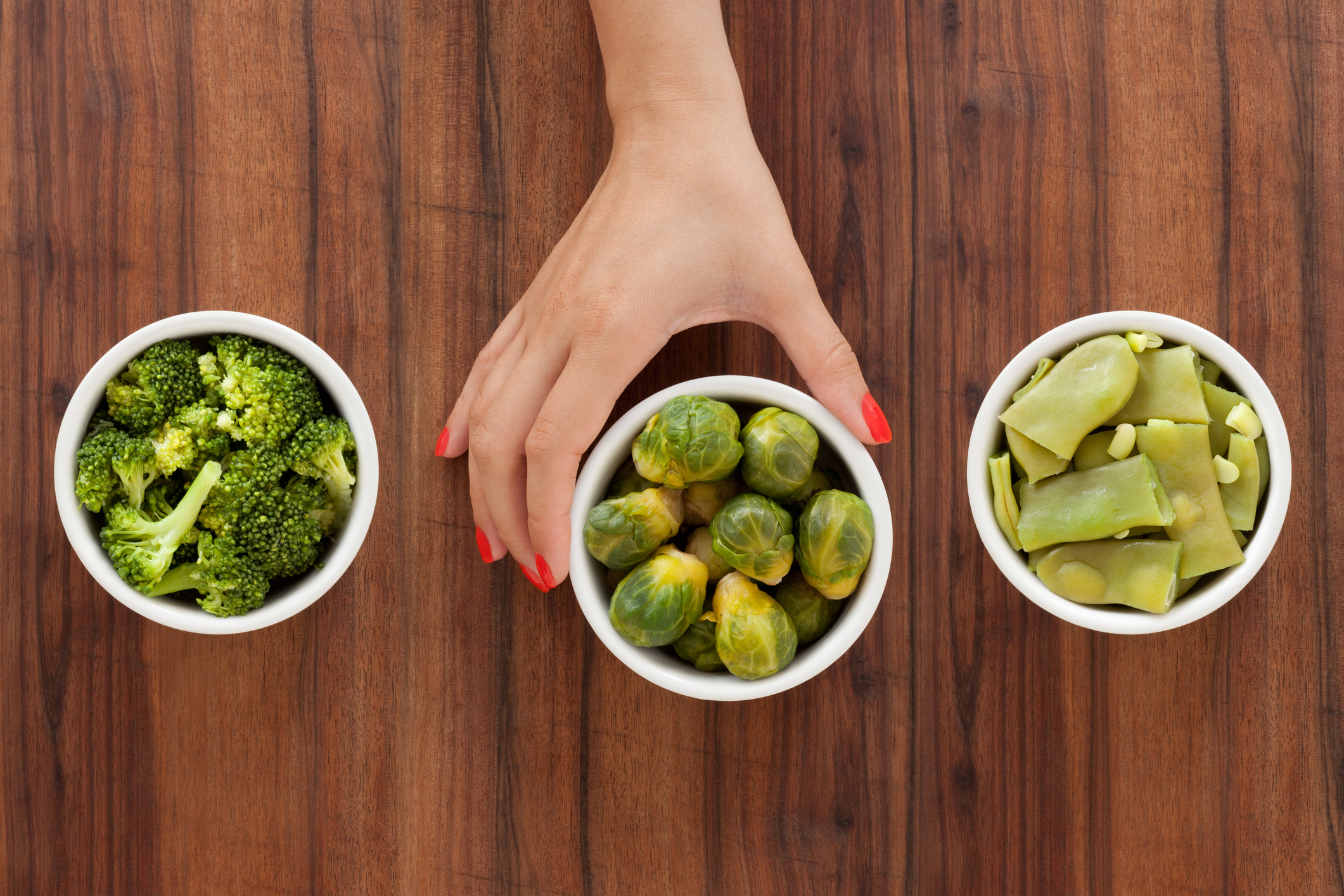 Three bowls with varieties of boiled vegetables and woman's hand holding the middle one