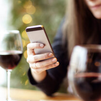 Kvinna kollar mobilen och dricker rött vin