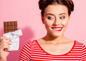 Ung kvinna mot rosa bakgrund håller i en chokladkaka