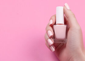 Hand med rosa naglar håller i rosa nagellack