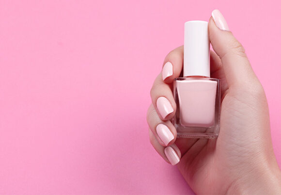 Hand med rosa naglar håller i rosa nagellack