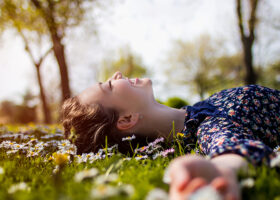 Ung kvinna ligger leende på rygg i gräset