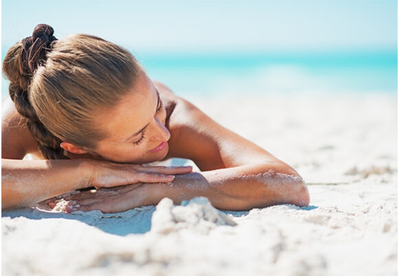 Kvinna solar på magen på sandstrand