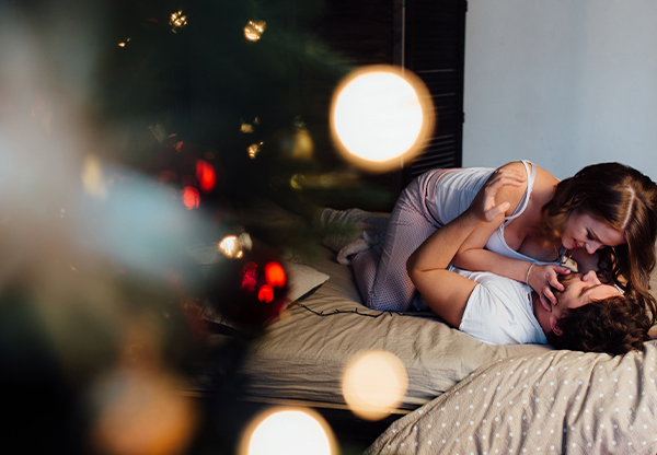 Par som hånglar i en säng bakom en julgran