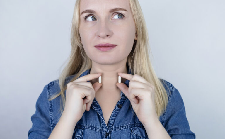 Närbild på kvinna som håller ett kosttillskott i varje hand framför halsen