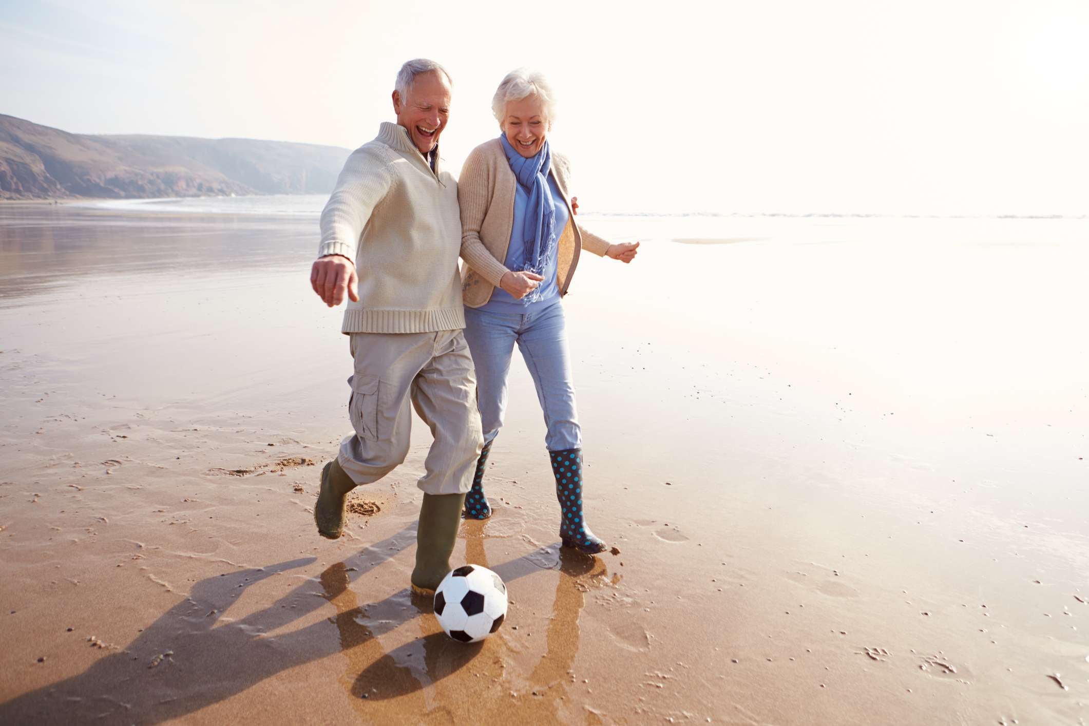 Äldre par spelar fotboll på stranden.
