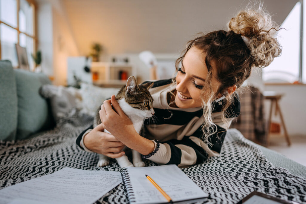 Ung kvinna som pluggare på sängen kramar om sin katt
