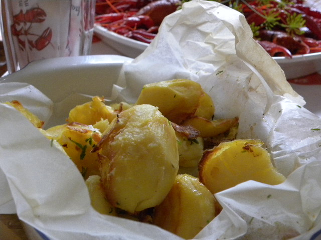 Ugnsbakad potatis i ett bakplåtspapper och kräftor i bakgrunden