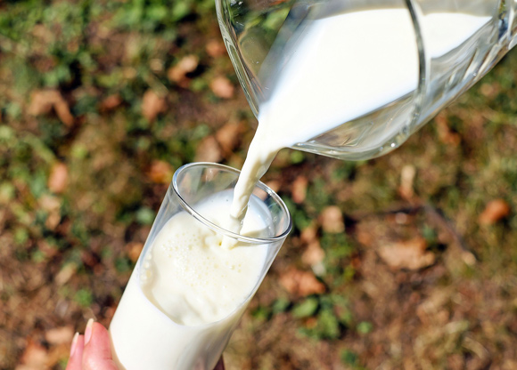 Hand häller mjölk från kanna till glas