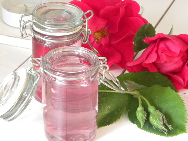 Rosenvatten på små glasflaskor med rosor i bakgrunden