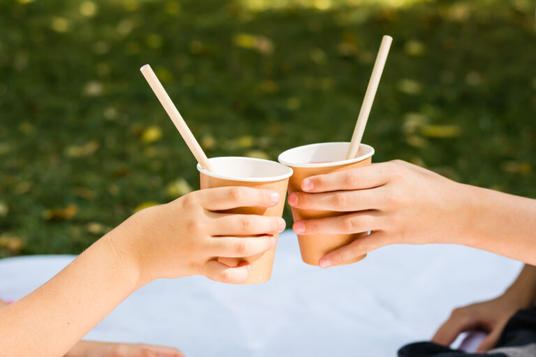 Två barns händer håller i pappmuggar med sugrör