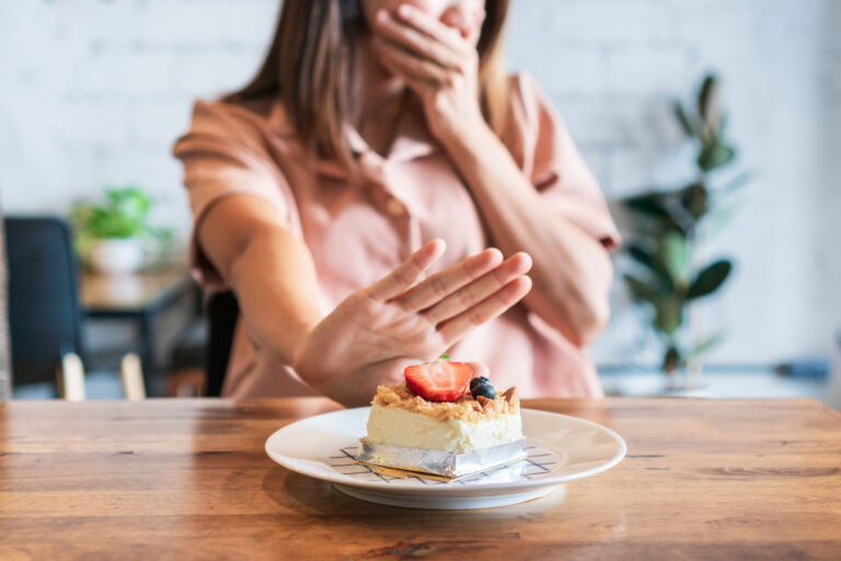 Ung kvinna håller för munnen och sätter handen framför en tårtbit