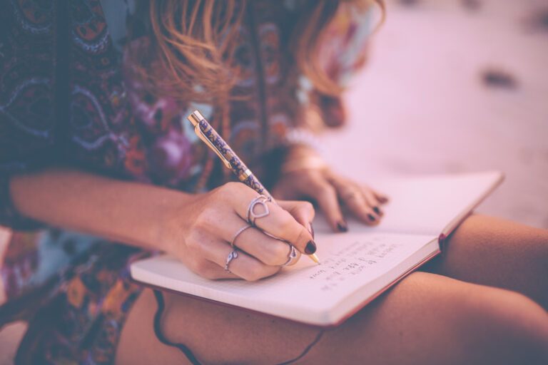 Beskuren bild på kvinna med långt hår som skriver dagbok med boken i knät