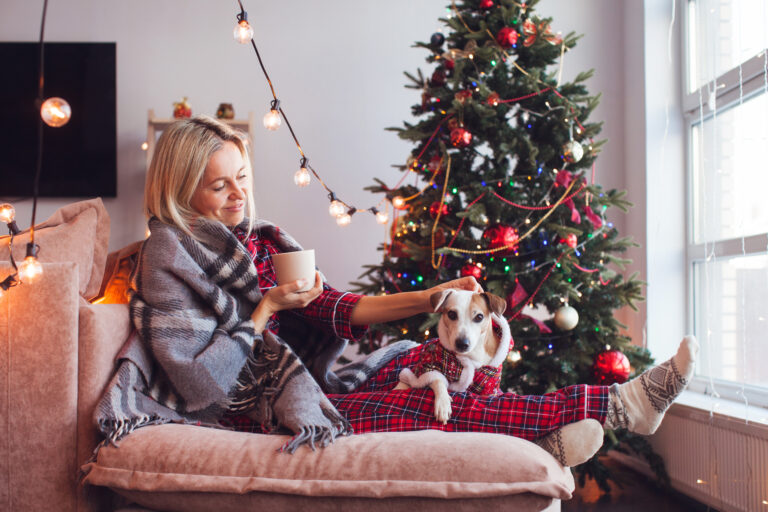 Kvinna sitter i soffan vid en julgran och klappar en hund