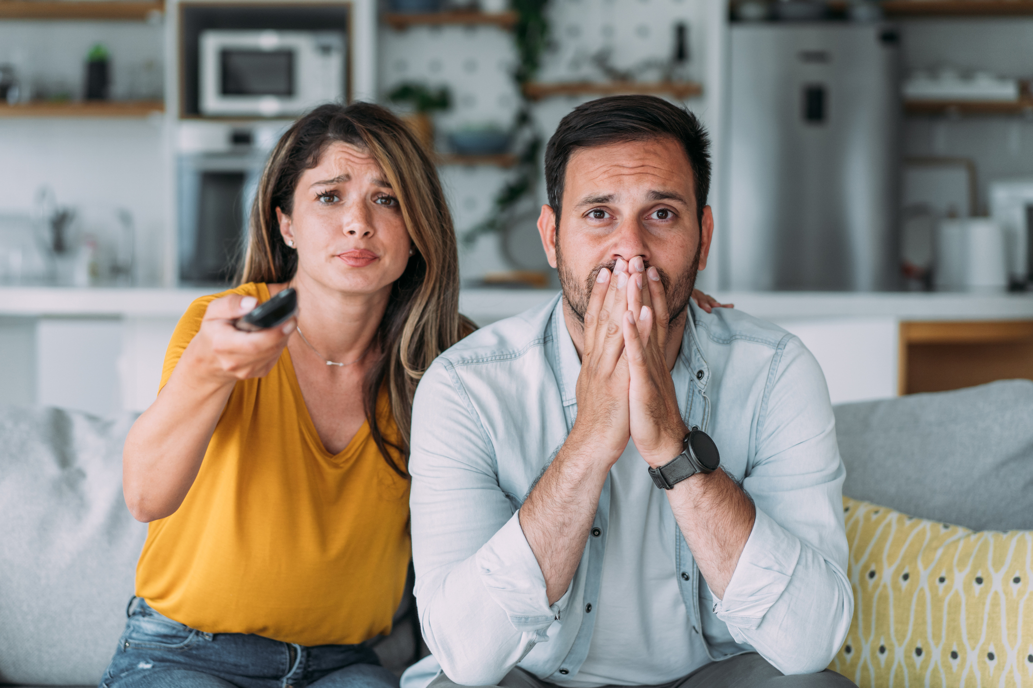 Man och kvinna i tv-soffan ser oroliga ut av att se på nyheterna