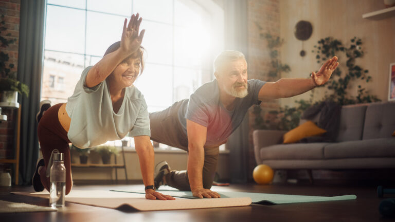 Medelålders par gör yogaövningar i hemmet