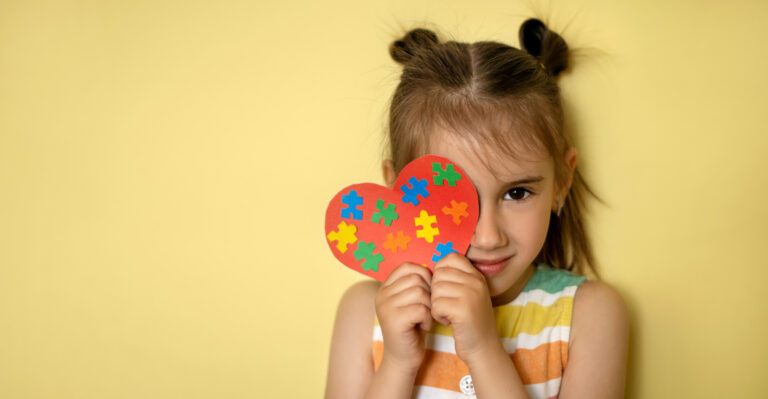 A beautiful girl holds a heart with colorful puzzles in her hands, covering one eye. World Autism Awareness Day. Banner