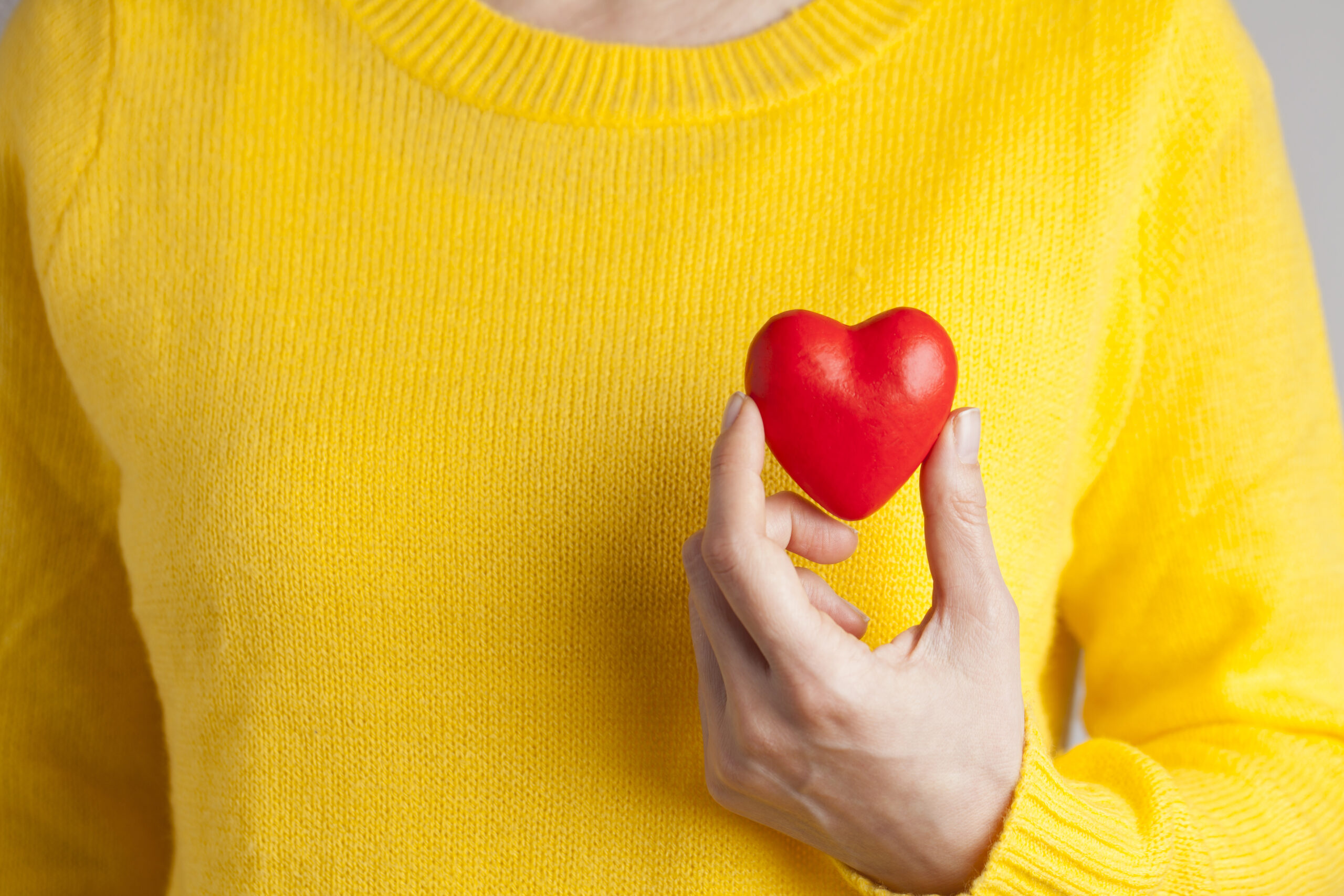 Närbild på kvinnlig hand som håller i litet rött gummihjärta mot en gul tröja
