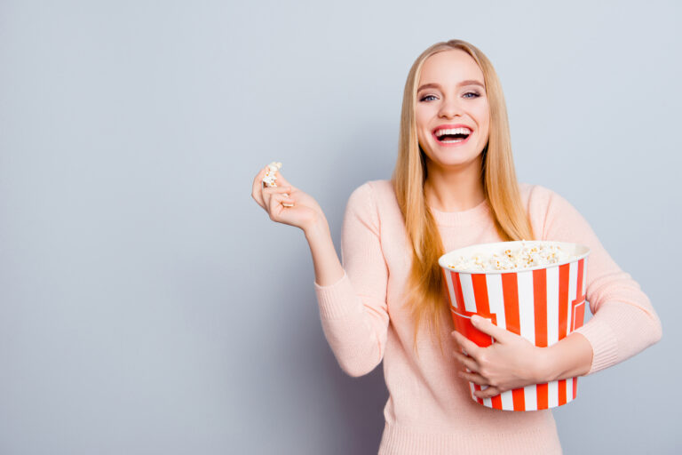 Leende ung kvinna äter popcorn ur rödvit kartong
