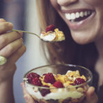 Närbild på leende kvinna som äter yoghurt med bär och müsli