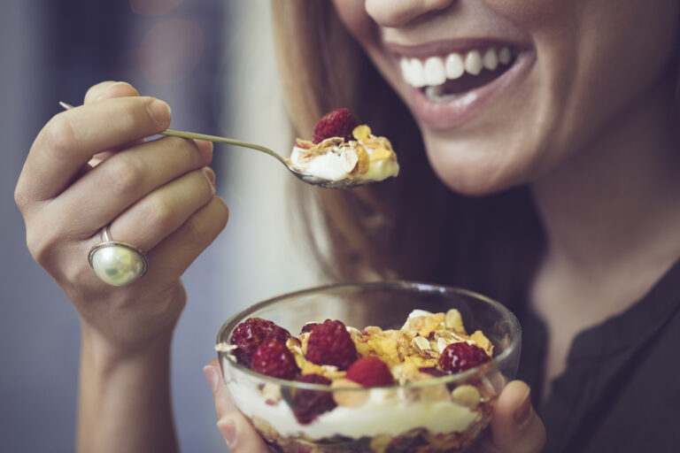 Närbild på leende kvinna som äter yoghurt med bär och müsli