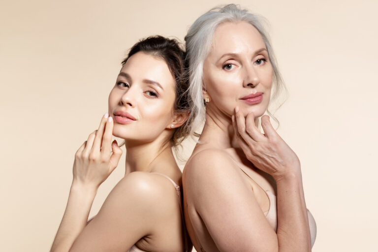 Elderly and young women with smooth skin and natural makeup standing back-to-back.