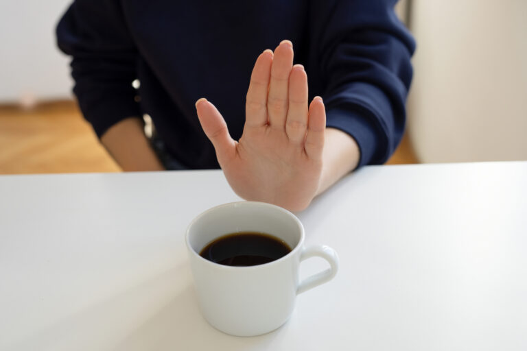 Hand som hålls upp framför en kopp kaffe, tackar nej