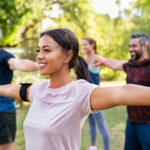 Group of multiethnic mature people stretching arms outdoor. Middle aged yoga class doing breathing exercise at park. Beautifil women and fit men doing breath exercise together with outstretched arms.
