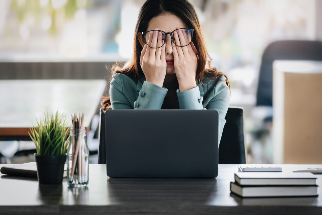 Stressad kvinna sitter vid skrivbord framför datorn med händerna för ansiktet