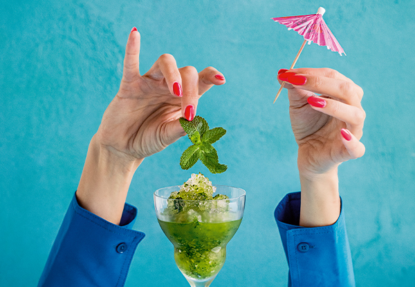 Mojito-drink i glas med is och händer som garnerar