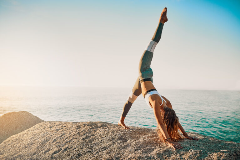 Kvinna står i yogaposition på klippa vid havet