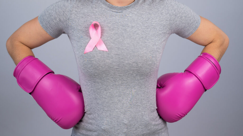 A faceless woman in pink boxing gloves with a pink ribbon holds her hands at her hips. Fight against breast cancer