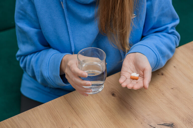 Närbild på kvinna som håller i ett glas vatten och tre tabletter att svälja