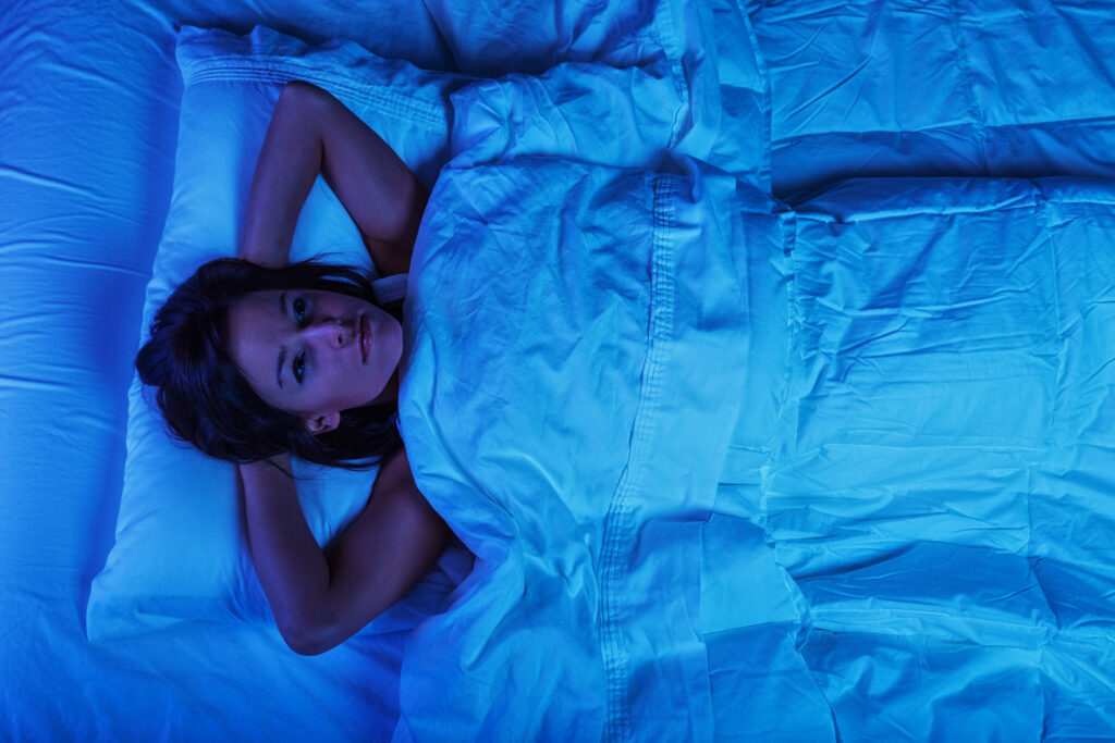 Photo of a young woman lying in bed at night, wide awake with a case of insomnia