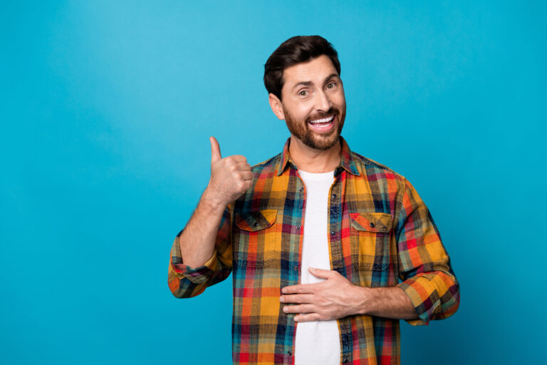 Photo portrait of nice young guy touch stomach good digestion show thumb up wear trendy plaid garment isolated on blue color background.