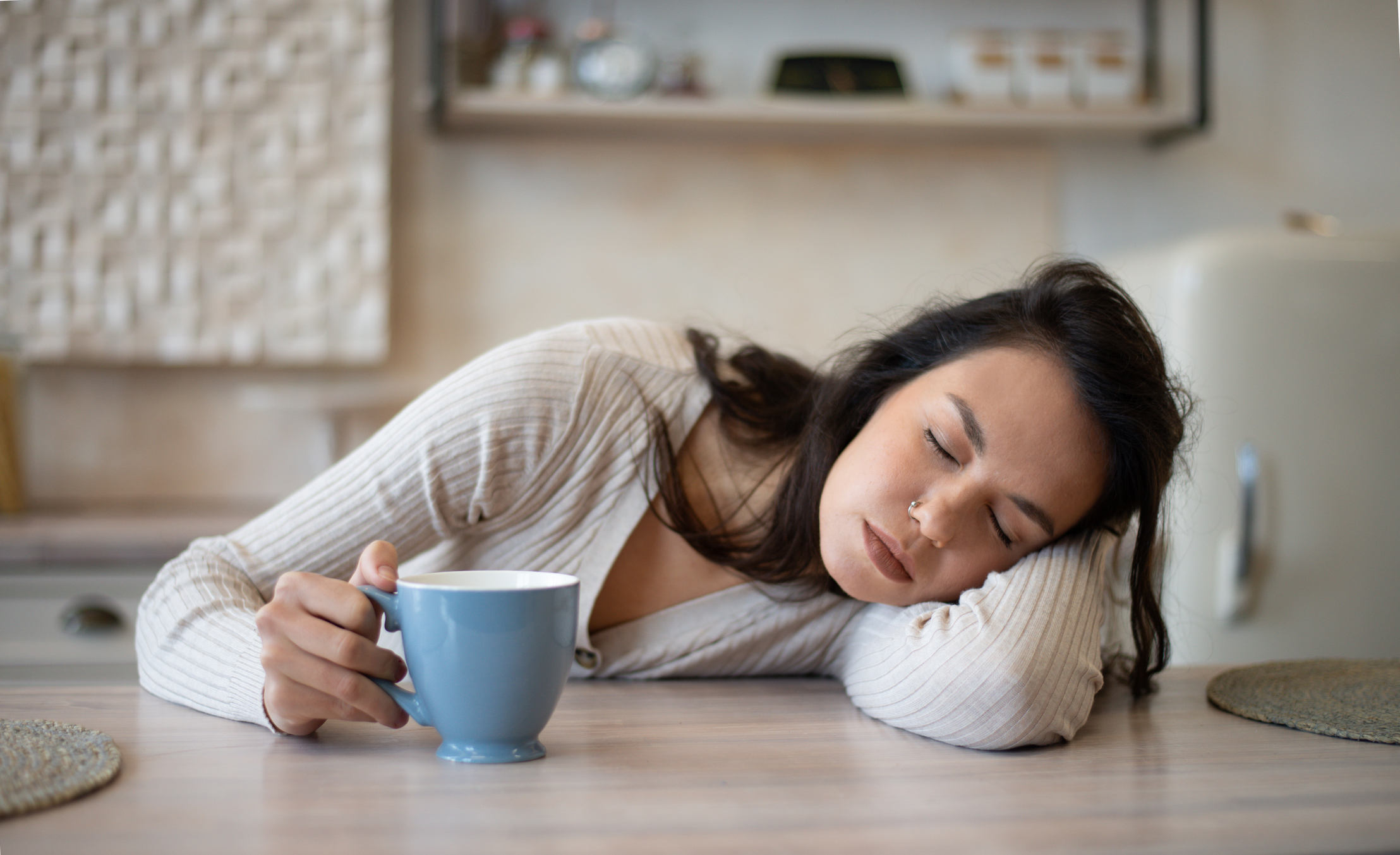 Ung kvinna sover vid matbordet med kaffekopp i handen