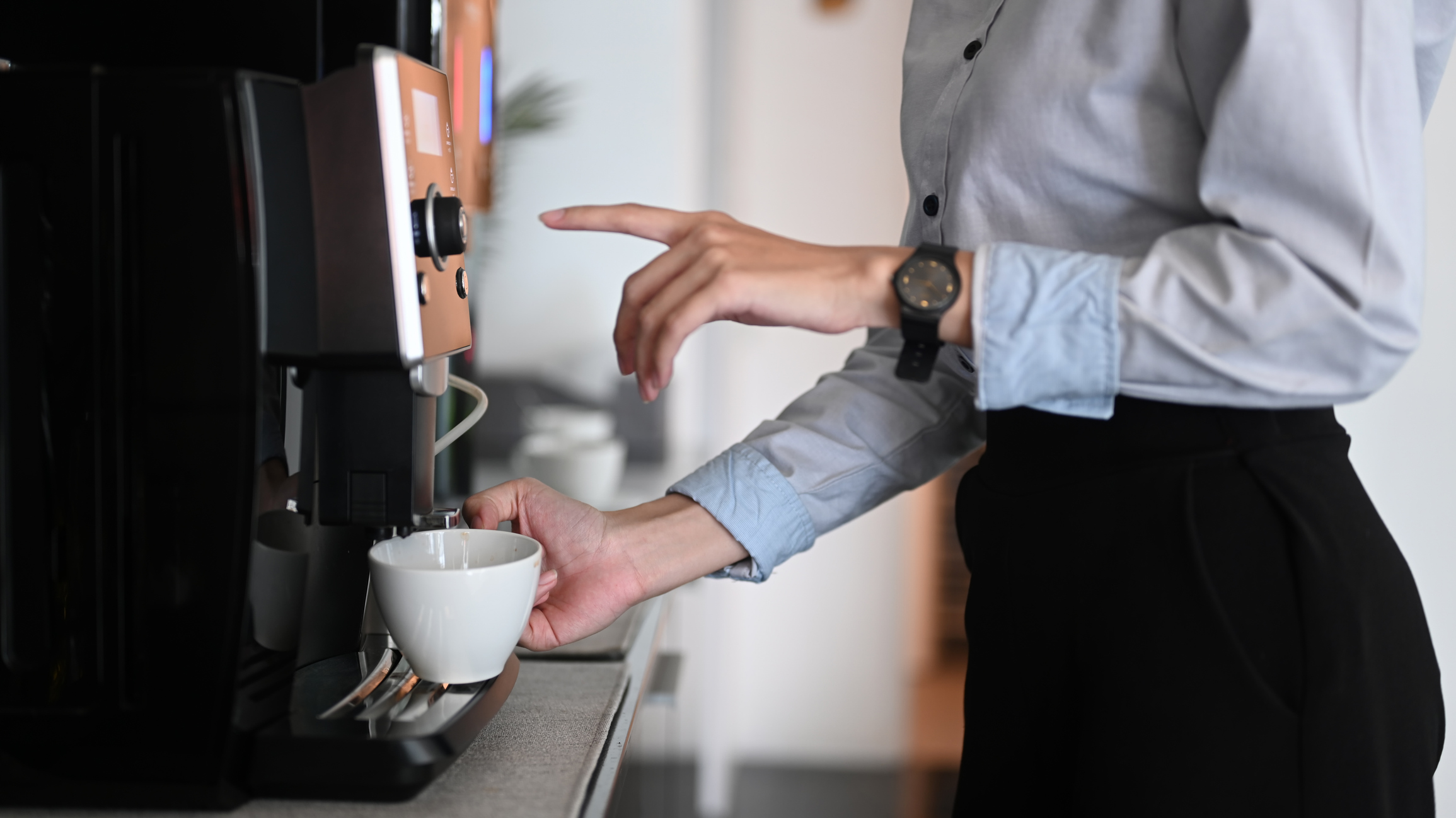 Kvinna trycker på knapp på en kaffemaskin på arbetsplats