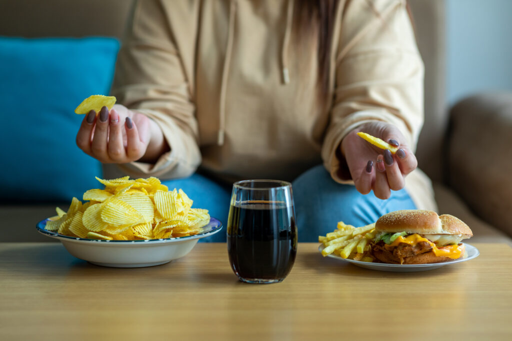 Närbild på kvinna i soffa som äter chips, skräpmat och dricker läsk