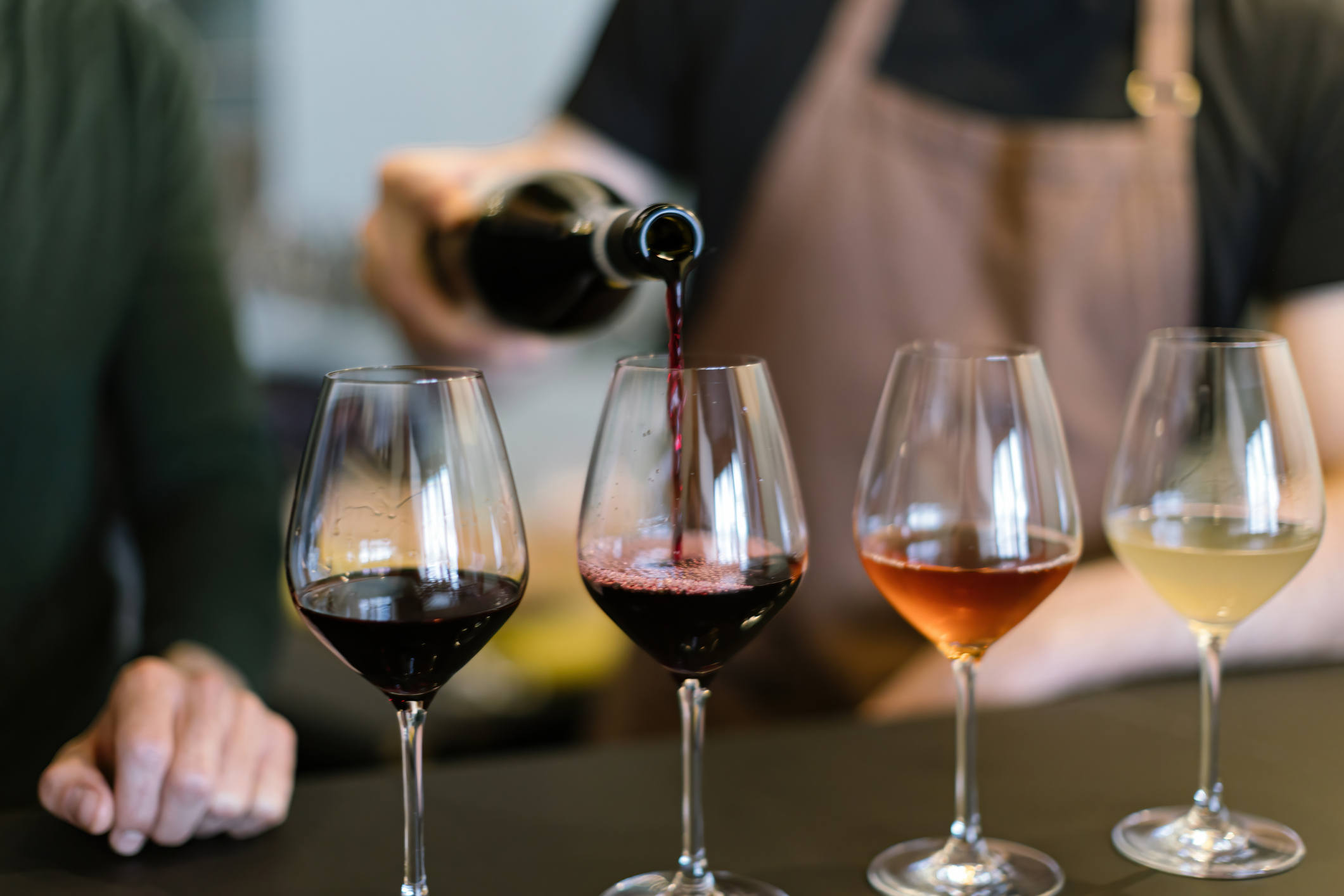 En hand håller i vinflaska och häller upp olika viner i fyra glas